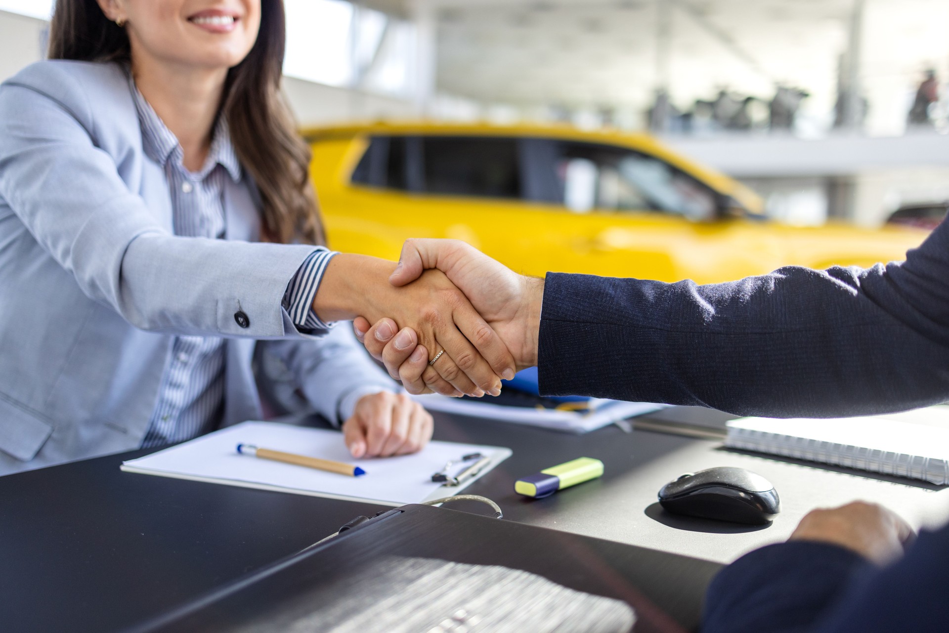 Car dealership, documents and people with handshake in showroom and contract, consulting and meeting. Man, woman and smile with legal agreement in sale for automobile, application and success in deal